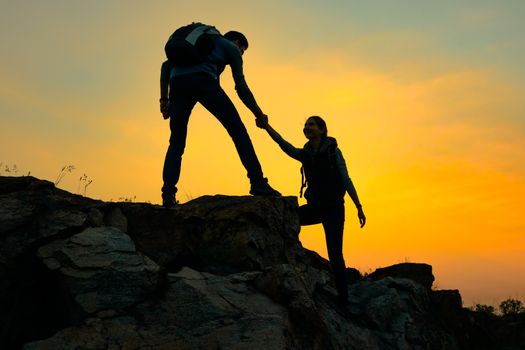 Travelers Hiking in the Mountains at Sunset. Man Helping Woman to Climb to the Top. Family Travel and Adventure.