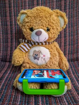 Burriana, Spain 08/09/2018:Brown teddy bear playing with a tablet