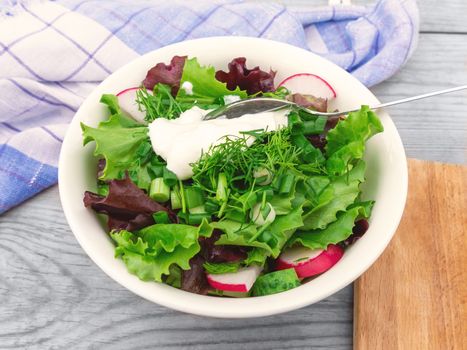 Summer vegetable salad with sour cream in a white bowl on a wooden table close-up