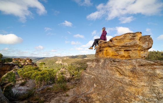 A bushwalker takes a break and admires splendid views in a landscape of pagodas, valleys, gullies, caves and canyons