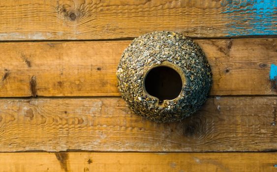 cylinder shaped bird house decorated with pebble stones, bird home hanging on a wooden wall