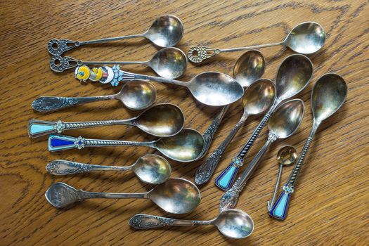 A pile of vintage, decorative spoons on an oak table