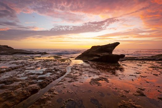Sunrise on coastal beach rock shelf with reflections low tide