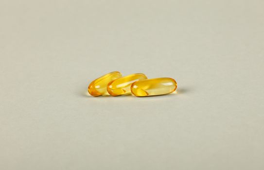 Close up three gel cap pills Omega 3 over grey