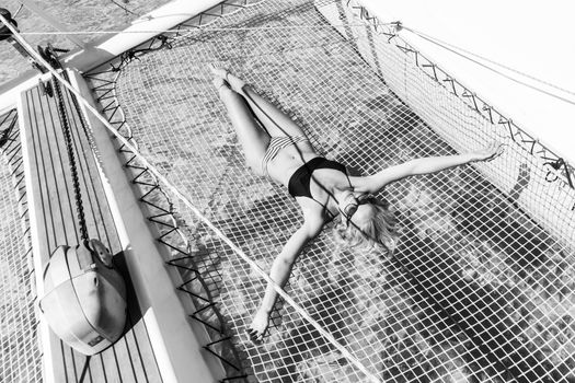 Womanin bikini tanning and relaxing on a summer sailin cruise, lying in hammock of luxury catamaran boat.