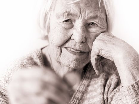 Sad elderly woman sitting at the table at home and looking miserably at only remaining coin from pension in her hand.