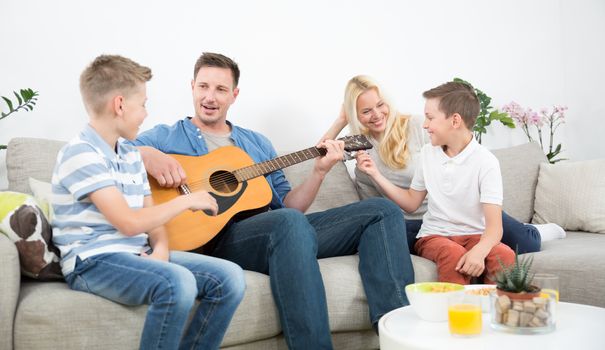 Happy caucasian family smiling, playing guitar and singing songs together at cosy modern home