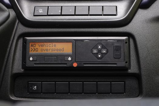 Digital tachograph display reads Vehicle Overspeed. No personal data. Tachograph in a van