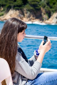 A young girl with long hair looks into the phone while sitting on a pleasure boat.