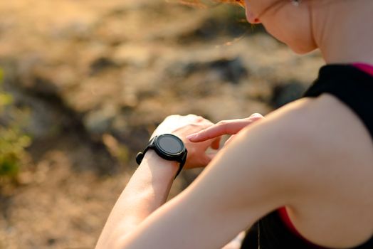 Young Woman Runner Using Multisport Smartwatch at Sunset Trail. Closeup of Hand with Fitness Tracker. Sports Concept.