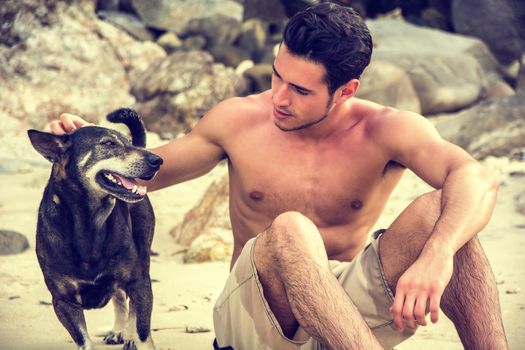 Young shirtless man on beach with a dog