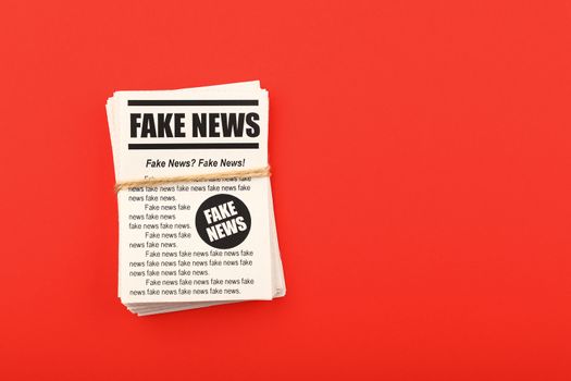 Stack of FAKE NEWS newspapers over red