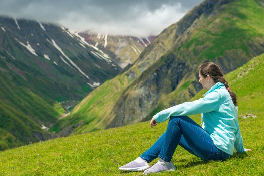A woman sits on the grass and admires the beautiful mountain lan