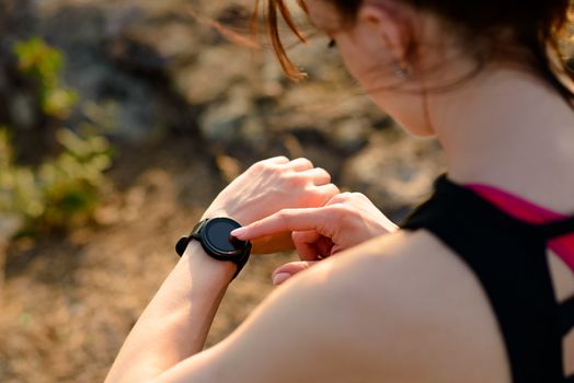 Young Woman Runner Using Multisport Smartwatch at Sunset Trail. Closeup of Hand with Fitness Tracker. Sports Concept.
