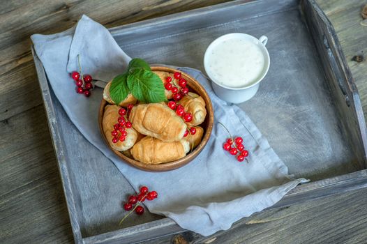 Croissants with currant berries on a wooden tray. The concept of a wholesome breakfast.