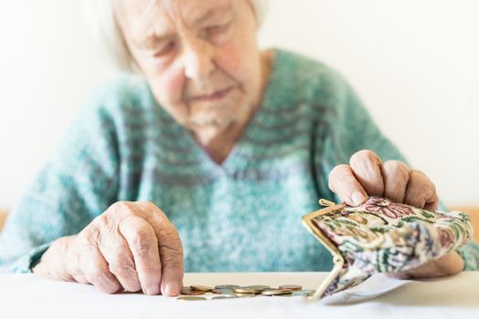 Concerned elderly woman sitting at the table counting money in her wallet.