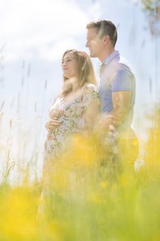 Young happy pregnant couple hugging in nature.
