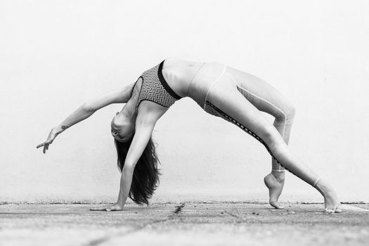 Fit sporty active girl in fashion sportswear doing yoga fitness exercise in front of gray wall, outdoor sports, urban style. Black and white photo.