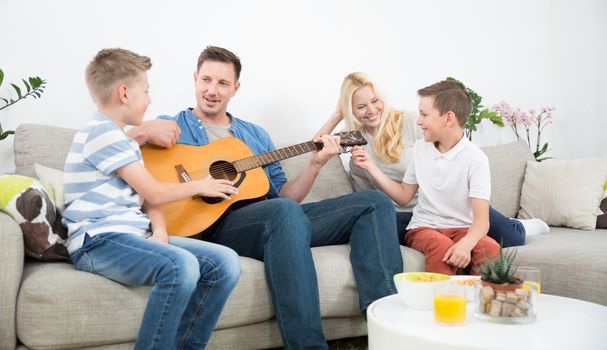 Happy caucasian family smiling, playing guitar and singing songs together at cosy modern home