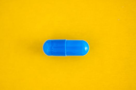 one blue pill capsule isolated on yellow background, close-up, top view, copy space
