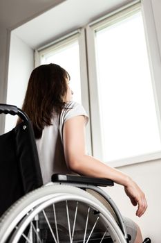 Invalid or disabled woman sitting wheelchair looking window daylight