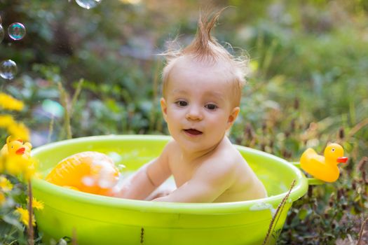 Toddler boy in basin taking a bath with bubbles and duck toys ou