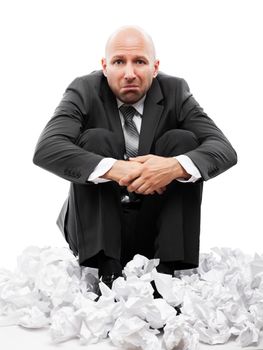 Businessman in depression sitting on crumpled torn paper document