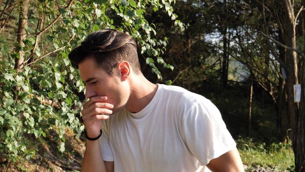 Young man coughing in nature in white t-shirt