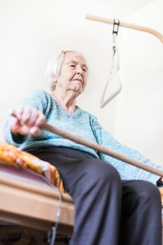 Elderly 96 years old woman exercising with a stick sitting on her bad.