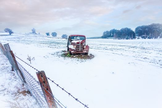 Rusty old car sits in a snow covered rural field