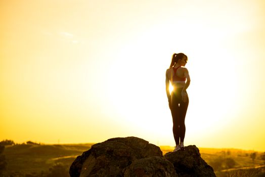 Young Woman Standing on the Rock at Hot Beautiful Summer Sunset. Adventure and Healthy Active Lifesyle Concept.