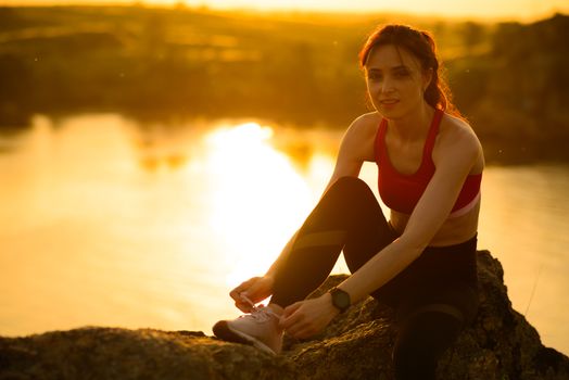 Young Sports Woman Tying Running Shoes and Preparing for Trail Run at Sunset. Healthy Lifestyle and Sport Concept.