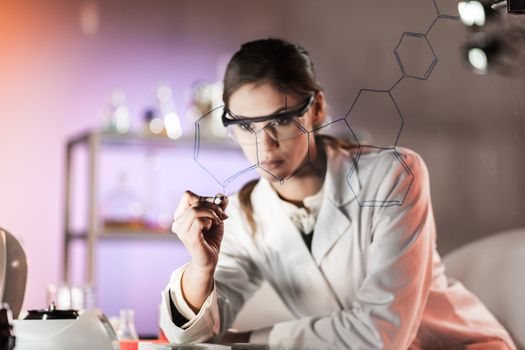 Portrait of a confident female researcher in life science laboratory writing structural chemical formula on a glass board.