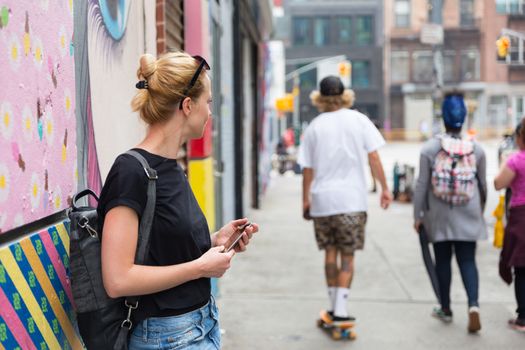 Woman using smartphone against colorful graffiti wall in New York city, USA.