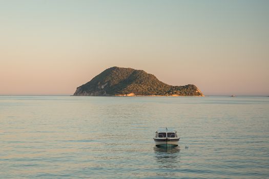 Seaside view of the Marathonisi or Turtle island near Greek island Zakynthos in the Ionian Sea wuht a boat in front of it.