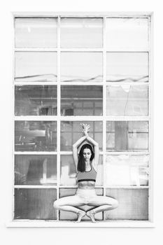 Fit sporty active girl in fashion sportswear doing yoga fitness exercise in front of big industrial window frame. colorful reflections in window glass. Urban style yoga. Black and white