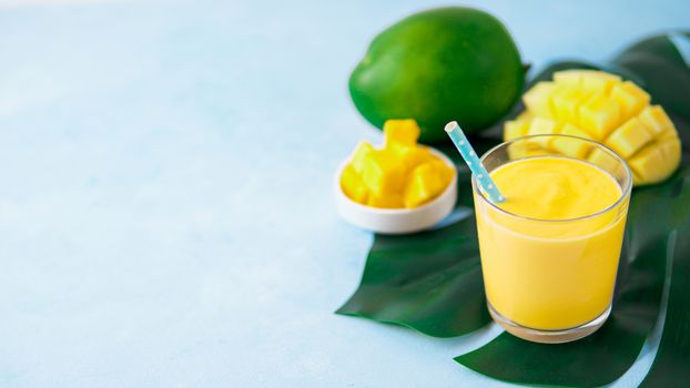 Yellow mango lassi milkshake on blue, sopy space