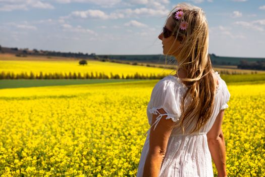 Woman in white dress standing by fields of golden canola