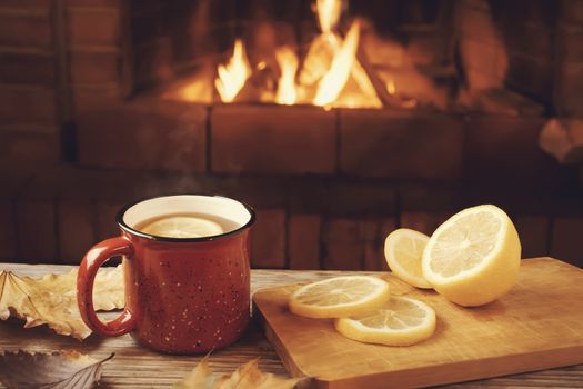 Red mug with hot tea with lemon in front of a burning fireplace, comfort and warmth of the hearth concept