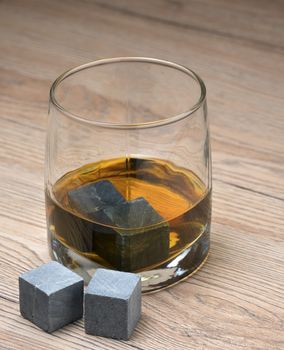 Stones in glass of whiskey on wooden background.