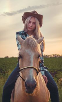 young girl dressed in a cowboy hat and blue jeans sits on a hors