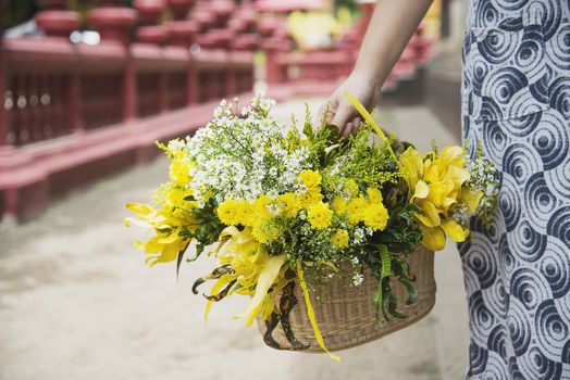 Asian lady holding fresh yellow flowers basket for participation local traditional Buddhist  ceremony - people with religion relationship concept