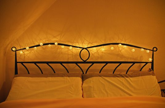 Romantic cozy bed with garland of lights around headboard