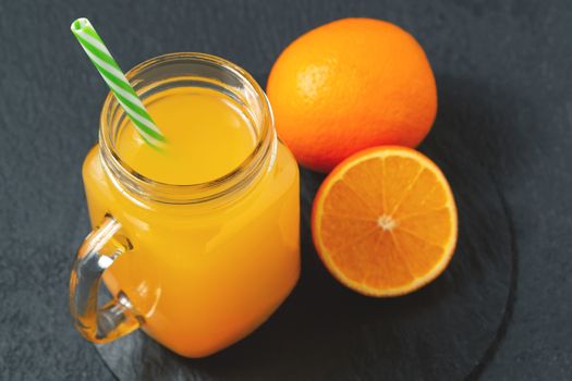 Homemade freshly squeezed orange juice in a Masonic jar and oranges on a black background