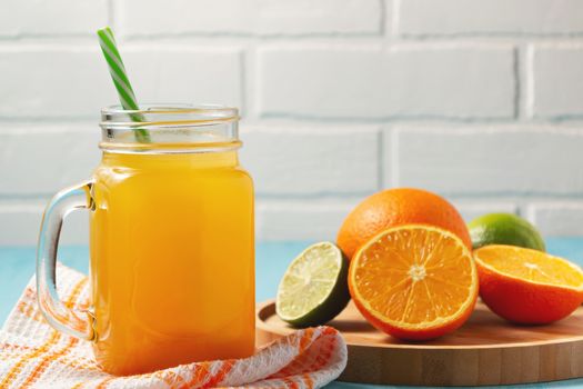 Homemade freshly squeezed orange juice in a mason jar, oranges and lime on wooden dish closeup, copyspace