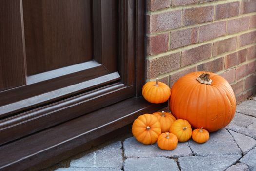 Large orange pumpkin and mini pumpkins as seasonal decorations at the front door of a house