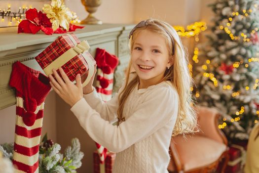 Cute teen girl with present near Christmas tree smiiling