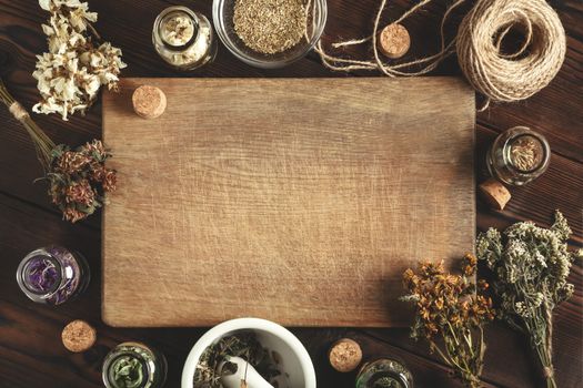 Cutting wooden board with various dried medicinal herbs and devices. Homeopathy and herbal treatment concept, place for text, copy space, top view, flat lay