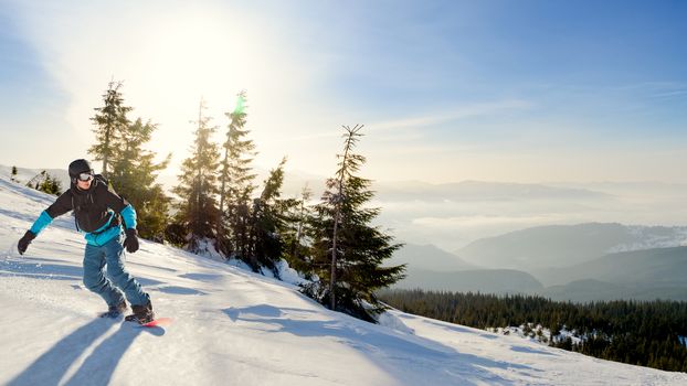 Young Snowboarder Riding Red Snowboard in Mountains at Sunny Day. Snowboarding and Winter Sports