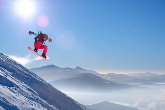 Snowboarder Jumping on Red Snowboard in Mountains at Sunny Day. Snowboarding and Winter Sports